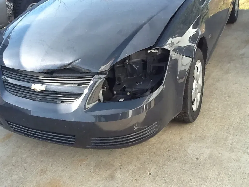 Damaged black car with a missing headlight and dented front fender.